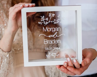 May include: A white frame with a clear glass insert. The glass has a floral design and the text "Morgan and Braden 05.31.2024" etched into it.