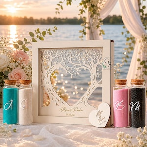 Op de afbeelding: Een houten trouwzandceremonieset. De set bevat een decoratief houten frame met een boomontwerp en een hartvormige uitsparing, gepersonaliseerd met namen en een datum. Het bevat ook glazen flessen gevuld met gekleurd zand.