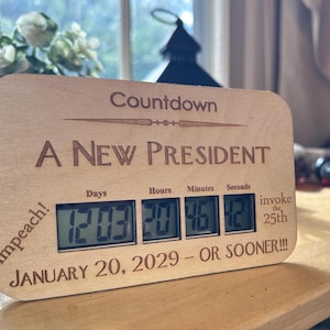 May include: Wooden countdown clock with the text "A NEW PRESIDENT" and digital display showing days, hours, minutes, and seconds. The clock also includes the text "impeach!" and "invoke the 25th". The date "JANUARY 20, 2029 - OR SOONER!!!" is also displayed.