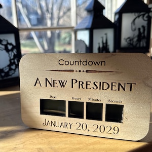May include: A wooden countdown clock with a black background and white text. The clock is counting down to a new president. The text on the clock reads "Countdown", "A New President", "Days", "Hours", "Minutes", "Seconds", and "January 20, 2029".