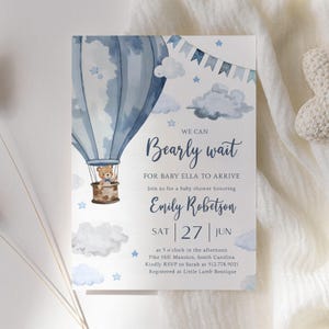 Può includere: Un invito a un baby shower con un design ad acquerello. L'invito presenta una mongolfiera blu con un orsacchiotto nel cestino, nuvole e stelle. Il testo recita "Bearly wait" e include il nome del bambino, la data e le informazioni RSVP.