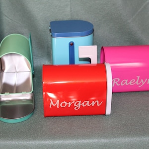 May include: Four colorful metal mailboxes with personalized names. The mailboxes are in shades of blue, green, red, and pink. The names "Morgan", "Raelyn" are visible on the mailboxes.