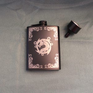 May include: Black metal flask with a silver dragon and dice design. The flask has a silver funnel.