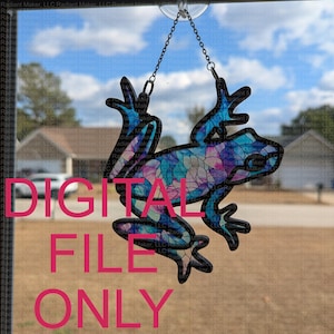 May include: A stained glass frog ornament with a blue, purple, and pink mosaic design. The frog is hanging from a chain and a suction cup.