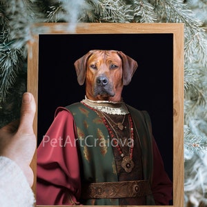 May include: A framed portrait of a dog dressed in a green and red medieval costume with gold accents. The dog is wearing a necklace with a large pendant and a crown. The background is black. The text "PetArtCraiova" is visible in the bottom left corner of the image.