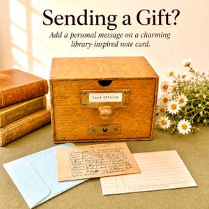 May include: A wooden card catalog drawer with a brass pull and label holder reading Card Catalog. Beside it are three stacked books, a light blue envelope, a handwritten index card, a lined note card, and a bouquet of white daisies.