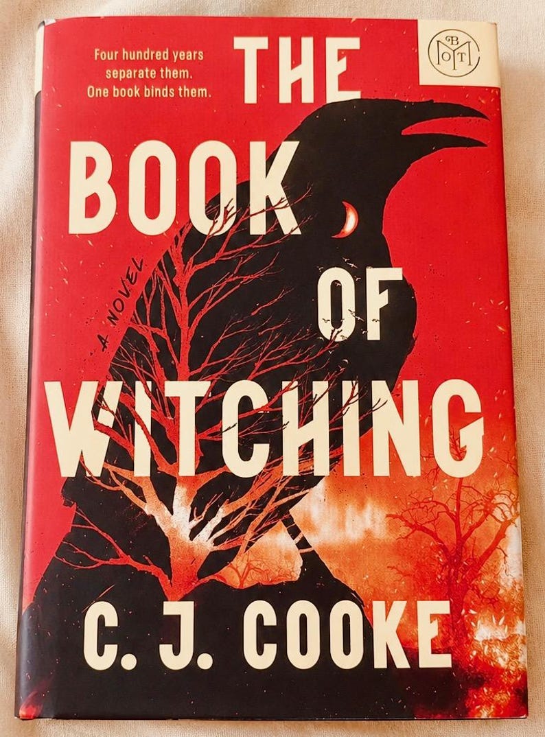 May include: A hardback book titled The Book of Witching by C. J. Cooke. The cover features a large black raven silhouette against a vibrant red background, with a bare red tree and the text: Four hundred years separate them. One book binds them.