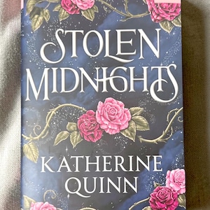 May include: A book titled Stolen Midnights by Katherine Quinn with a dark blue, starry night sky background. The cover features pink roses on thorny vines, a small pink square logo in the top right corner, and white serif lettering.