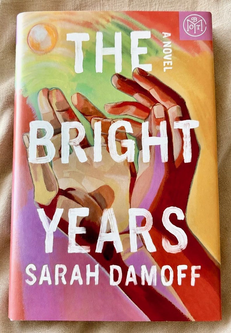 May include: A book titled The Bright Years by Sarah Damoff with a cover illustration featuring two hands reaching upward against a colourful background of orange, yellow, pink, and green. The title is printed in large white letters across the centre.