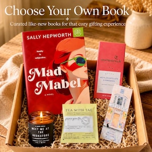 May include: A gift box containing the novel Mad Mabel by Sally Hepworth, a Moonstruck milk chocolate cinnamon bar, a Tea with Tae jasmine green tea sachet, a lit candle labeled Meet Me at the Bookstore, and a bookmark featuring a bookshop illustration.