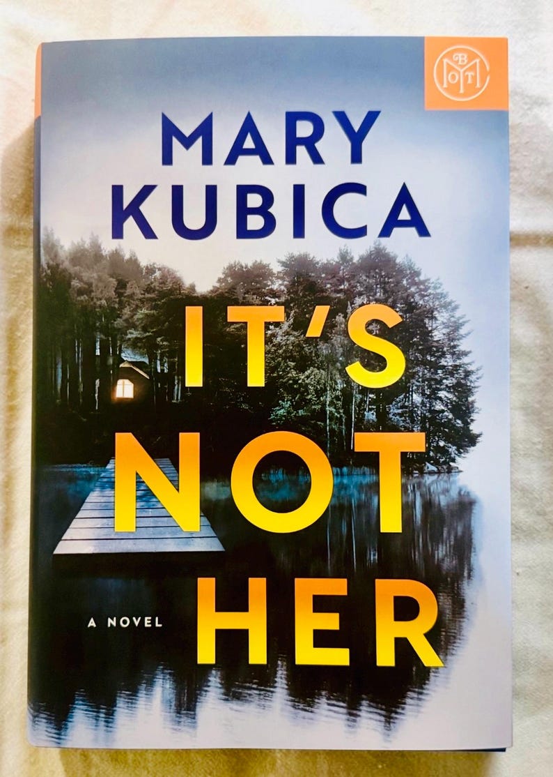May include: A book titled It's Not Her by Mary Kubica. The cover features a dark forest and a wooden dock extending into a lake at night, with a single glowing window visible in the trees. The title text is in large yellow and orange letters.