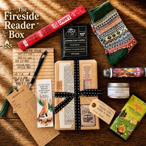 May include: A gift box set titled The Fireside Reader Box containing a red Chomps beef stick, a Copper Cow Coffee packet, a green patterned sock, a mini puzzle tube, a Black Coffee candle, a Campers Smores chocolate bar, a pen, a reading list card, and a wrapped book with a tag labeled blind date with a book.