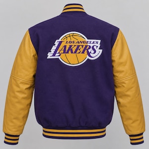 May include: A purple varsity jacket with gold leather sleeves and a large Los Angeles Lakers basketball team logo embroidered on the back. The jacket features a ribbed collar, cuffs, and hem with purple and gold stripes, and a button-up front.