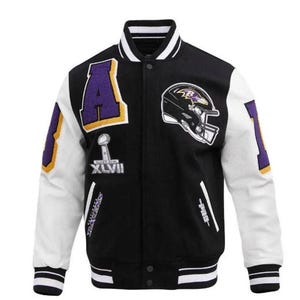 May include: A black and white varsity jacket featuring purple and gold patches. The front displays a large letter A, a football helmet, and a Super Bowl XLVII trophy graphic. The sleeves are white with purple patches, and the collar and cuffs have black and white stripes.