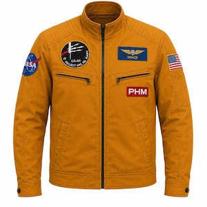 May include: A mustard yellow jacket featuring a central zipper, a stand-up collar, and quilted shoulder panels. It is adorned with various patches, including a NASA logo, a Project Hail Mary emblem, a Grace wing patch, a PHM label, and a US flag.