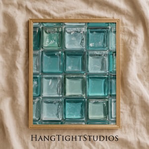 May include: A framed print with a gold-coloured frame, displaying a grid of teal and aqua glass blocks. The text "HANGTIGHTSTUDIOS" is printed in black at the bottom. The artwork is displayed on a beige fabric.