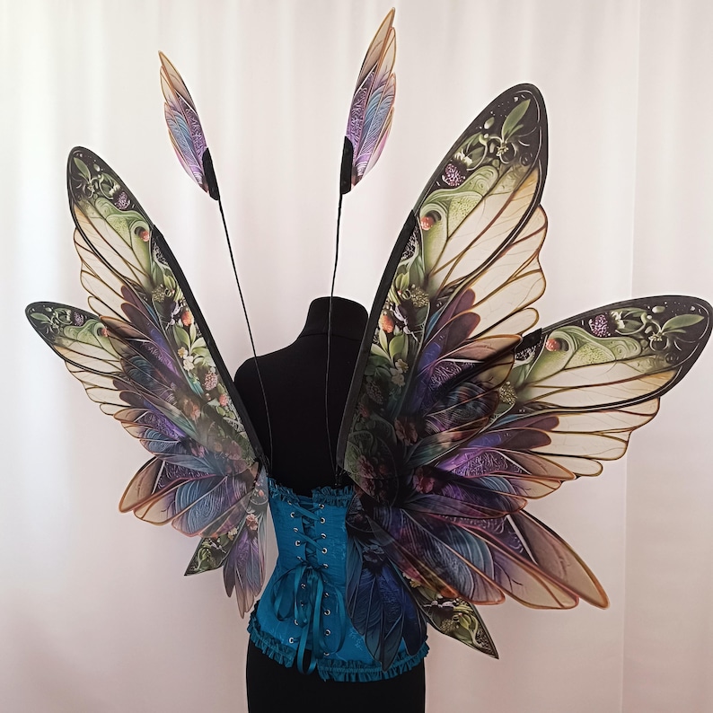The wings of the fairy have a beautiful floral pattern. You can see voluminous green leaves and autumn flowers.