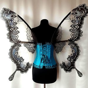 May include: A pair of black and white lace butterfly wings with a teal blue corset. The wings are made of sheer fabric with a delicate lace pattern.