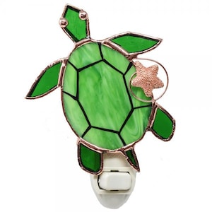 May include: A stained glass night light shaped like a green sea turtle with a copper starfish hanging from it. The night light has a white on/off switch.