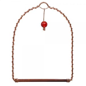 May include: A copper bird swing with a red bead hanging from the top. The swing is made of twisted wire and has a wooden perch.