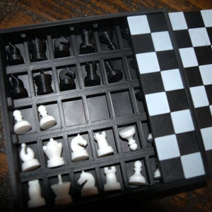 May include: A black and white chess set with a foldable board. The chess pieces are black and white, stored in a compartment within the box. The board is a classic checkerboard pattern.