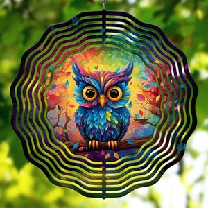 May include: A colorful metal wind spinner with a multi-layered design featuring an owl with bright blue, green, and purple feathers. The owl is perched on a branch with colorful leaves and a sunset background.
