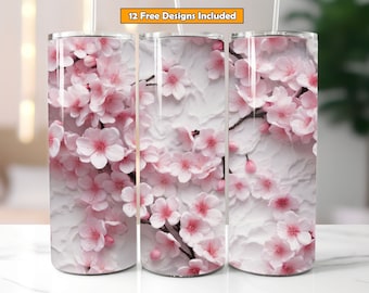 May include: Three stainless steel tumblers with a floral design. The design features pink cherry blossoms on a textured white background. The tumblers have a straw and the text "12 Free Designs Included".