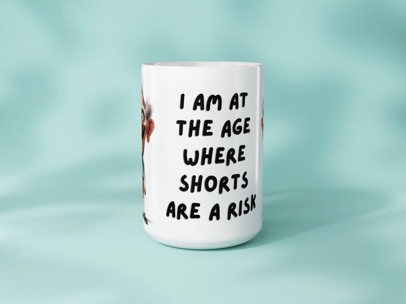 Mockup showing an 11oz or 15oz mug with a sublimation design depicting a humorous old man and the text I am at the age where shorts are a risk Set against a light blue background to illustrate how the design appears on a physical mug