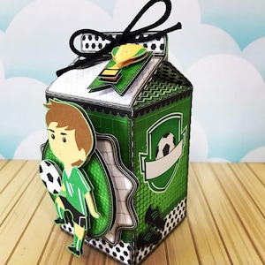 Puede incluir: Una caja de cartón verde y negra con forma de cartón de leche con un jugador de fútbol y un balón de fútbol en el lateral. La caja tiene una cinta negra atada alrededor de la parte superior.