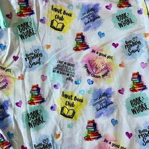 May include: White fabric with a colorful, watercolor-style pattern featuring stacks of books, hearts, and text. The text includes phrases like "Book Whore", "Smut Book Club", "Busy Reading Smut", and "I dust my shelves but my books are still filthy".