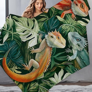 May include: A green, orange, and blue patterned throw blanket with a design of three lizards on a tropical leaf background.