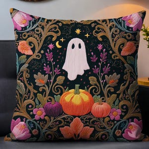 May include: Square decorative pillow with a Halloween theme. The pillow features a black background with a white ghost, pumpkins, flowers, and a crescent moon and stars design. The pillow is on a gray couch.