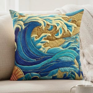 May include: Square decorative pillow featuring an embroidered design of a large ocean wave in shades of blue and gold. The pillow has a detailed, textured appearance, with the wave cresting over a golden background. The pillow is on a beige sofa.