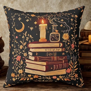 Peut inclure: Coussin décoratif noir orné d'une pile de livres, d'une bougie allumée et d'une fiole de potion. Le motif comprend des éléments floraux et célestes dorés et orangés, créant une ambiance mystique.