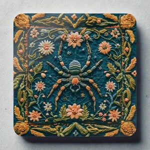 Puede incluir: Posavasos cuadrado con un diseño bordado detallado que presenta una araña en el centro, rodeada de flores y follaje. La paleta de colores incluye verde azulado, naranja y verde, creando un tema inspirado en la naturaleza.