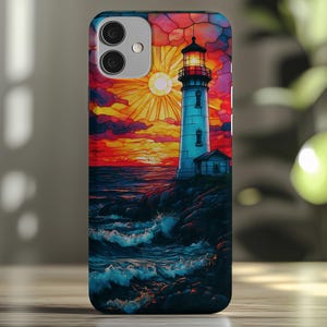 May include: A phone case with a stained glass design of a lighthouse on a rocky shore at sunset. The lighthouse is white with a red roof and a light on top. The sky is orange, pink, and purple. The waves are blue and white.