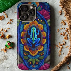 Puede incluir: Funda de teléfono colorida con un diseño bordado detallado. La funda presenta una rana azul en el centro, rodeada por un intrincado patrón de elementos florales naranjas, amarillos y azules. La funda tiene un acabado brillante.
