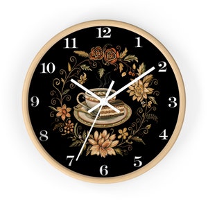 May include: A black and white clock with a wooden frame. The clock face features a floral design with a cup of coffee and a slice of cake in the center. The numbers 1 through 12 are displayed around the clock face.