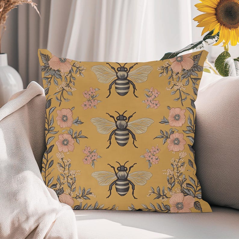 May include: A yellow throw pillow with a floral pattern and bees. The pillow has a repeating pattern of pink flowers, green leaves, and black and white bees.