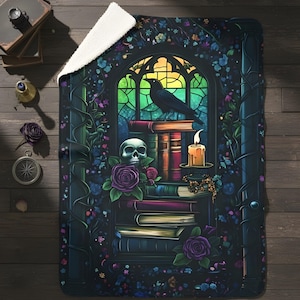May include: A dark-colored throw blanket with a gothic design. The image features a raven perched on books in front of a stained-glass window. A skull, roses, and a lit candle are also depicted. The blanket has a white, fluffy underside.