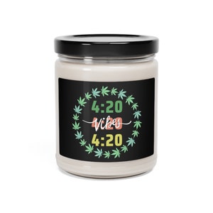 Puede incluir: Una vela blanca en un tarro de vidrio con una etiqueta negra. La etiqueta tiene una corona de hojas de marihuana verde, amarilla y azul con el texto "4:20 Vibes 4:20" en el centro.
