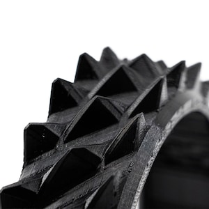 May include: Close-up of a black, ring-shaped object with a series of sharp, triangular spikes. The object has a textured surface and appears to be made of a rigid material. The spikes are evenly spaced around the ring.