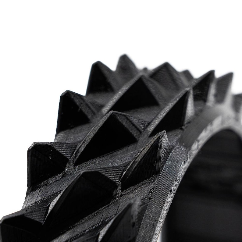 May include: Close-up of a black, ring-shaped object with a series of sharp, triangular spikes. The object has a textured surface and appears to be made of a rigid material. The spikes are evenly spaced around the ring.