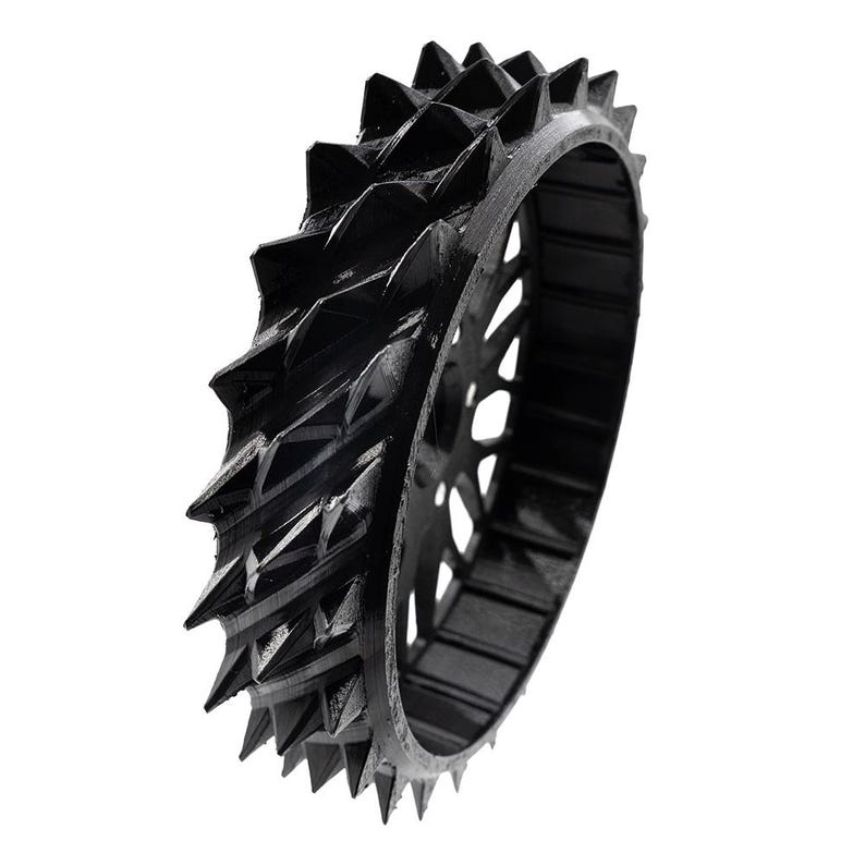 May include: A black, spiky gear wheel with a series of triangular protrusions around the outer edge. The wheel has a series of holes in the center. The gear is set against a white background.
