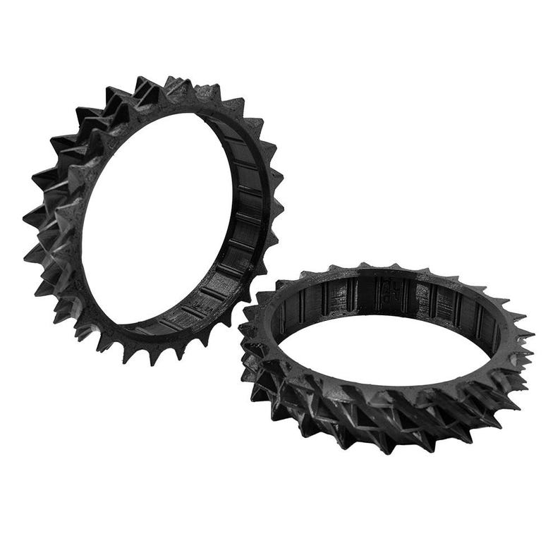 May include: Two black, circular objects with a spiked, gear-like design. The objects are made of a matte material and are positioned against a white background. The objects appear to be 3D-printed.