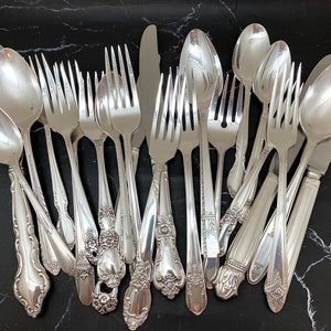 May include: A collection of vintage silverware, including forks, spoons, and a butter knife, all with ornate handles. The silverware is made of polished silver and has a classic, elegant design.