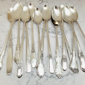 May include: A set of ten silver-plated spoons with ornate designs. The spoons are all the same size and shape, and they have a long, slender handle.
