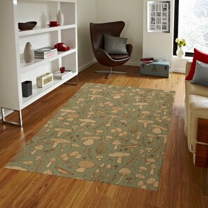 May include: A green and brown area rug with a mushroom pattern. The rug is in a living room with a white bookshelf, a brown leather egg chair, and a white couch.