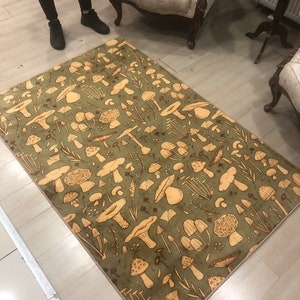 May include: A green and beige area rug with a mushroom pattern. The rug has a beige border and features a variety of mushroom shapes and sizes.