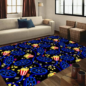 Puede incluir: Una alfombra rectangular con fondo negro con un patrón repetido de carretes de película azules y cubos de palomitas de maíz rojos y blancos. Granos de palomitas de maíz amarillas están dispersos por el diseño. La alfombra está en un salón.